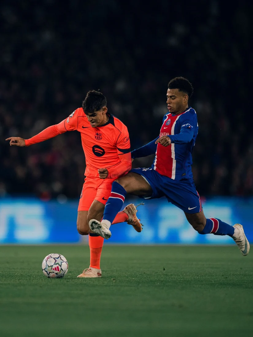 Lamine Yamal strikes the ball with a PSG defender challenging