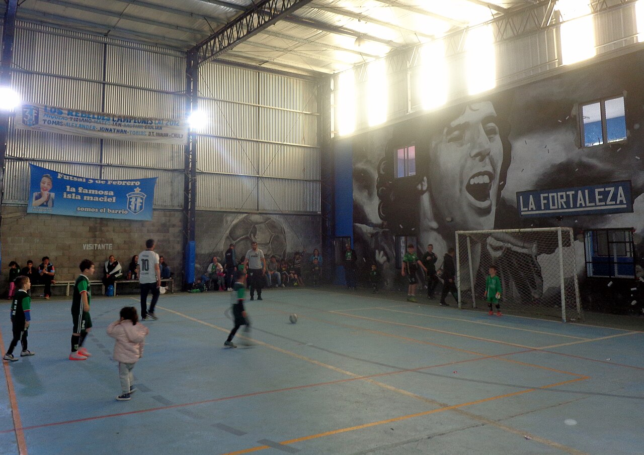 Young children playing baby fútbol on a hard indoor court at Polideportivo 3 de Febrero in Dock Sud, Buenos Aires