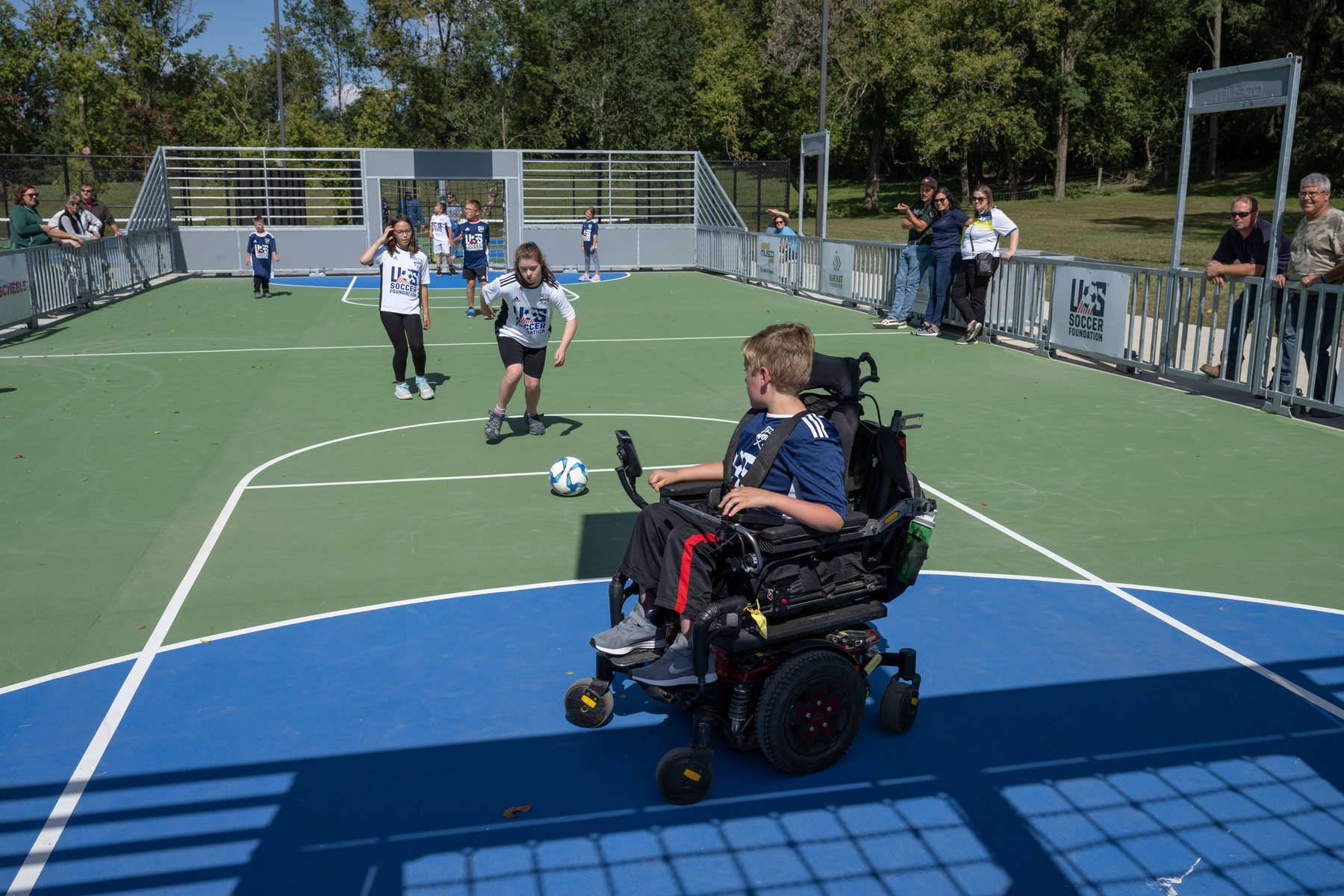 Children, including a power-wheelchair player, play together on an accessible mini-pitch